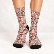 Front view of retro cowgirl socks worn against a clean white studio background. Detailed pink and green western print features cowboy boots, oversized bows, wildflowers, hearts, and horseshoes with black toe accents.