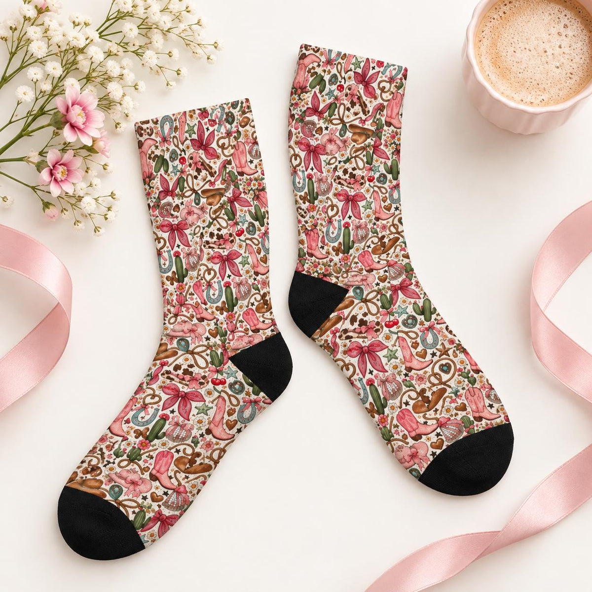 Vintage western crew socks arranged flat on a cream background with pink ribbon, delicate flowers, and a coffee mug. Colorful all-over pattern showcases cowboy boots, horseshoes, cactus illustrations, and pink bows.
