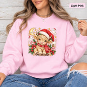 Light Pink Gildan 18000 sweatshirt featuring a cute Christmas Highland cow in a Santa hat and red scarf surrounded by candy canes, holly, stars, and festive greenery.