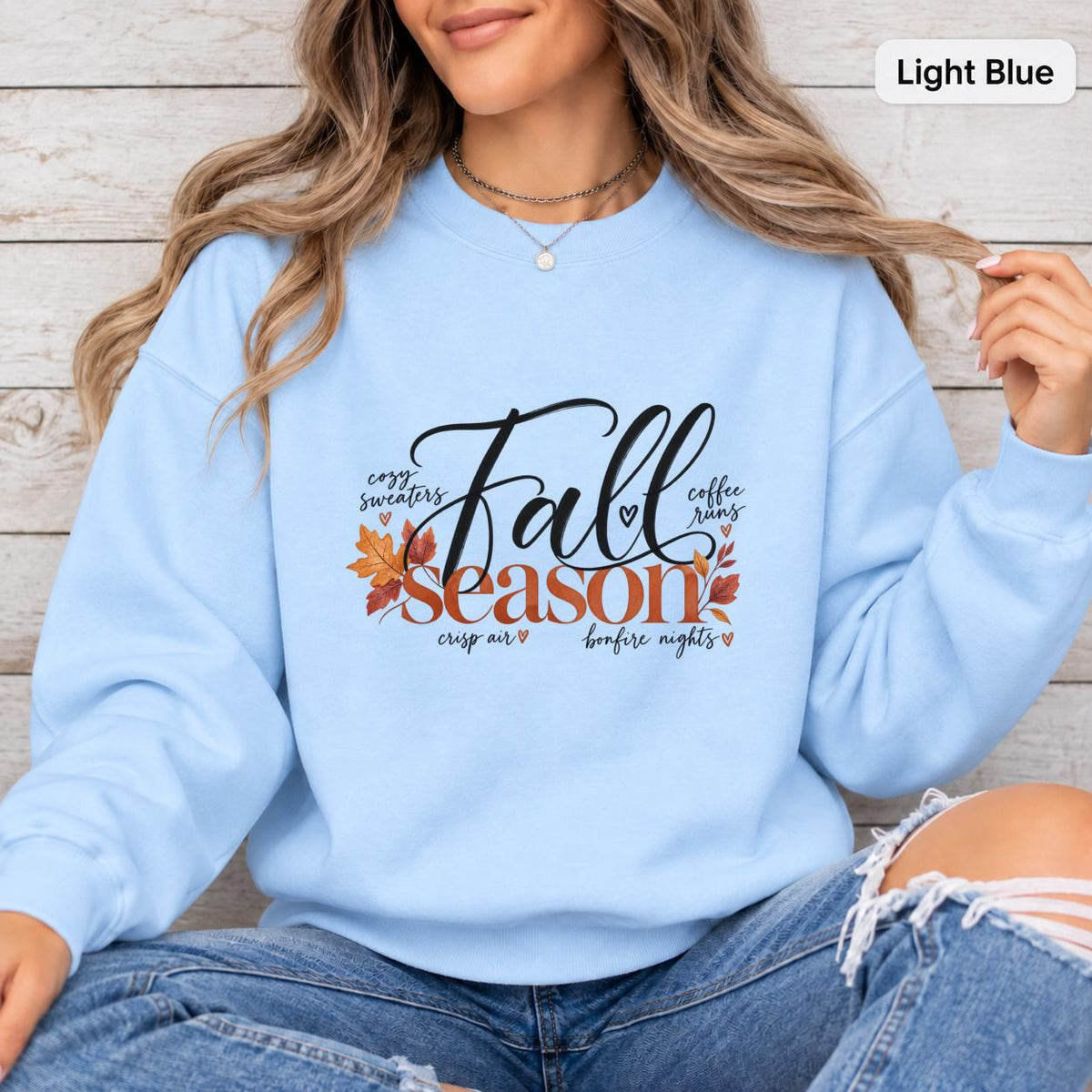 Light Blue Gildan sweatshirt featuring the black and burnt orange Fall Season artwork with leaf accents and cozy seasonal details.
