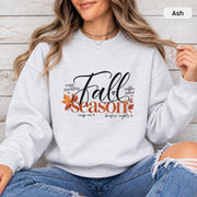 Ash Gildan 18000 crewneck showing the Fall Season graphic with elegant script text, warm autumn leaves, and fall-inspired phrases.