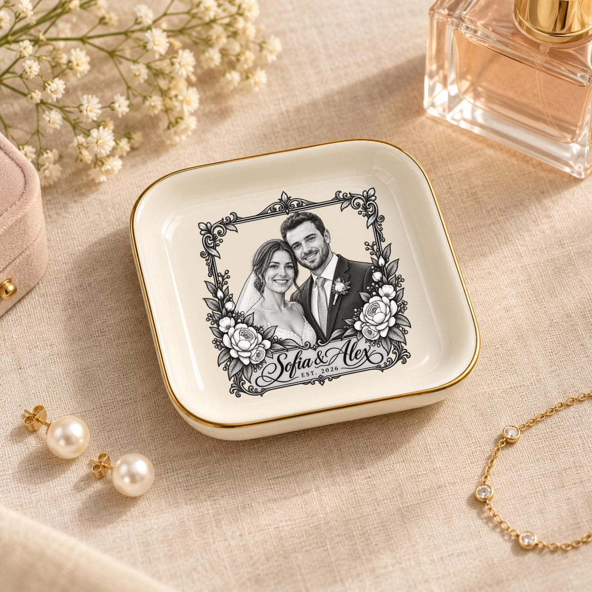 Custom wedding jewelry dish displayed with perfume and delicate accessories on a warm neutral surface, featuring a personalized couple portrait and vintage floral border.