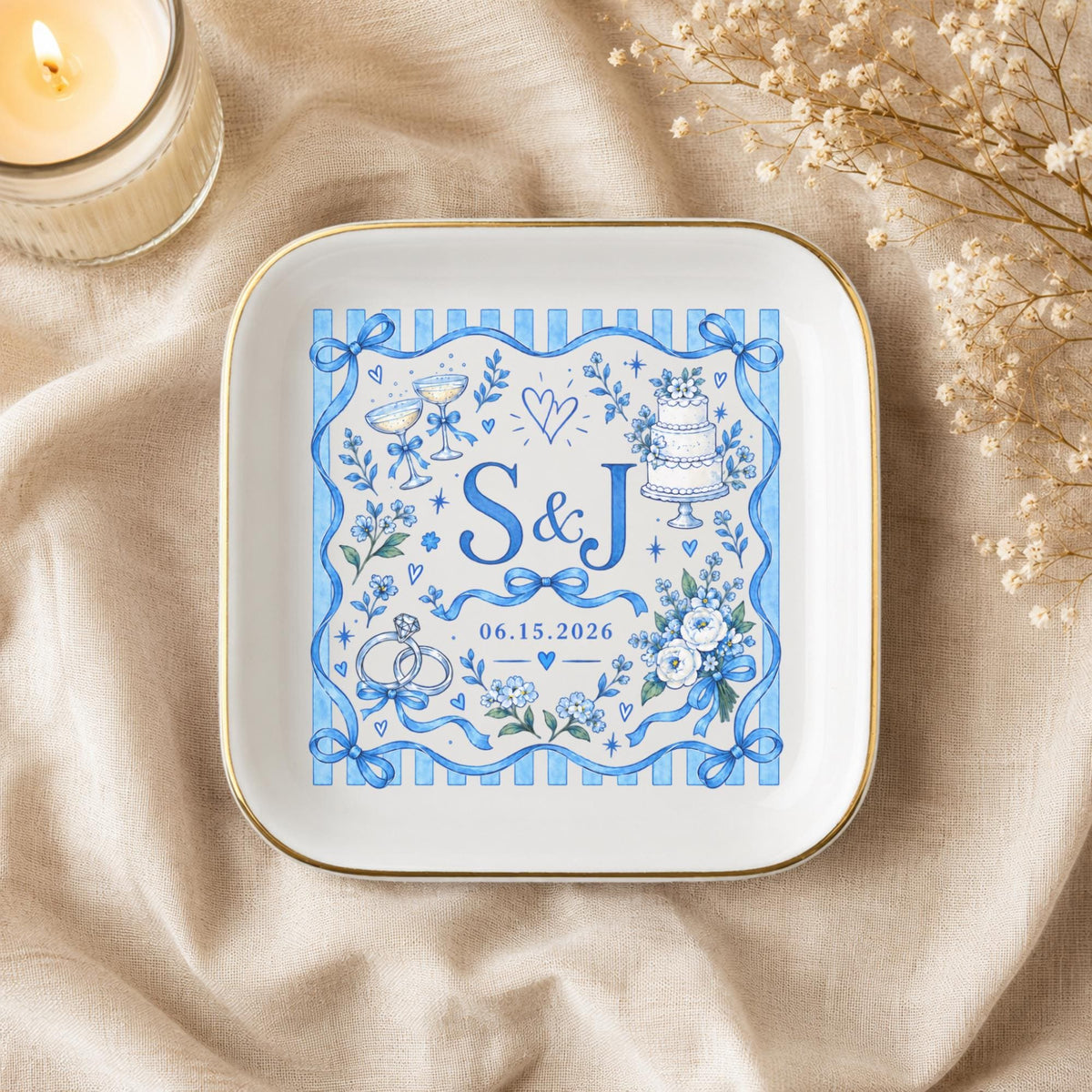Custom wedding jewelry dish styled on champagne satin with soft neutral accents, gold trim, and a blue monogram design with initials S and J.