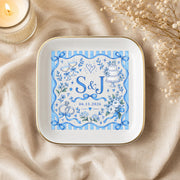 Custom wedding jewelry dish styled on champagne satin with soft neutral accents, gold trim, and a blue monogram design with initials S and J.