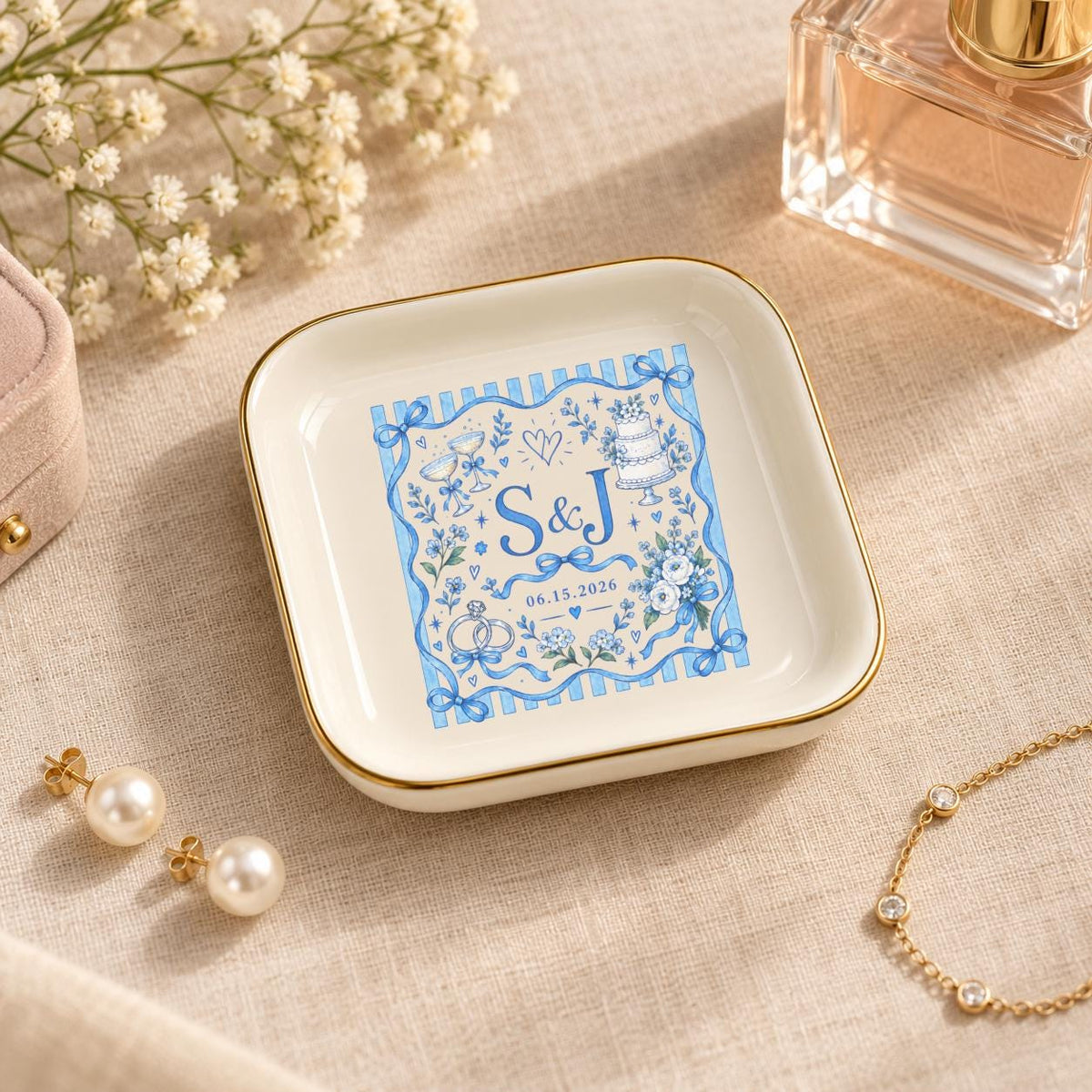 Custom ceramic jewelry dish displayed with perfume and delicate accessories on a warm neutral surface, featuring a blue personalized wedding motif and gold trim.