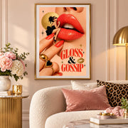 Framed retro lipstick poster hanging above a cream sofa with blush pink cushions. The colourful surreal artwork features a miniature glamorous woman sitting beside oversized red lips, with gold celestial accents and bold Gloss and Gossip lettering.