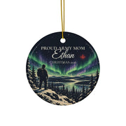 Printify product mockup of the round ceramic ornament with gold string, showing a soldier on a snowy ridge under green northern lights and the example lettering Proud Army Mom, Ethan, Christmas 2026