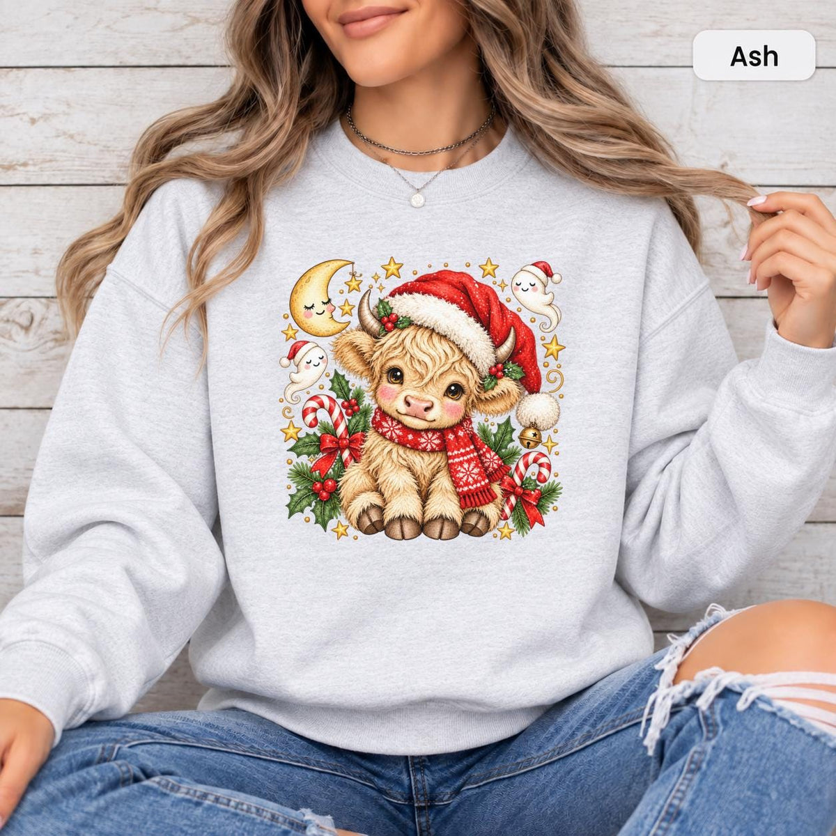 Ash Gildan 18000 crewneck showing the festive cow artwork with warm neutral fur tones, red holiday accessories, greenery, and gold stars.