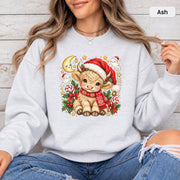 Ash Gildan 18000 crewneck showing the festive cow artwork with warm neutral fur tones, red holiday accessories, greenery, and gold stars.