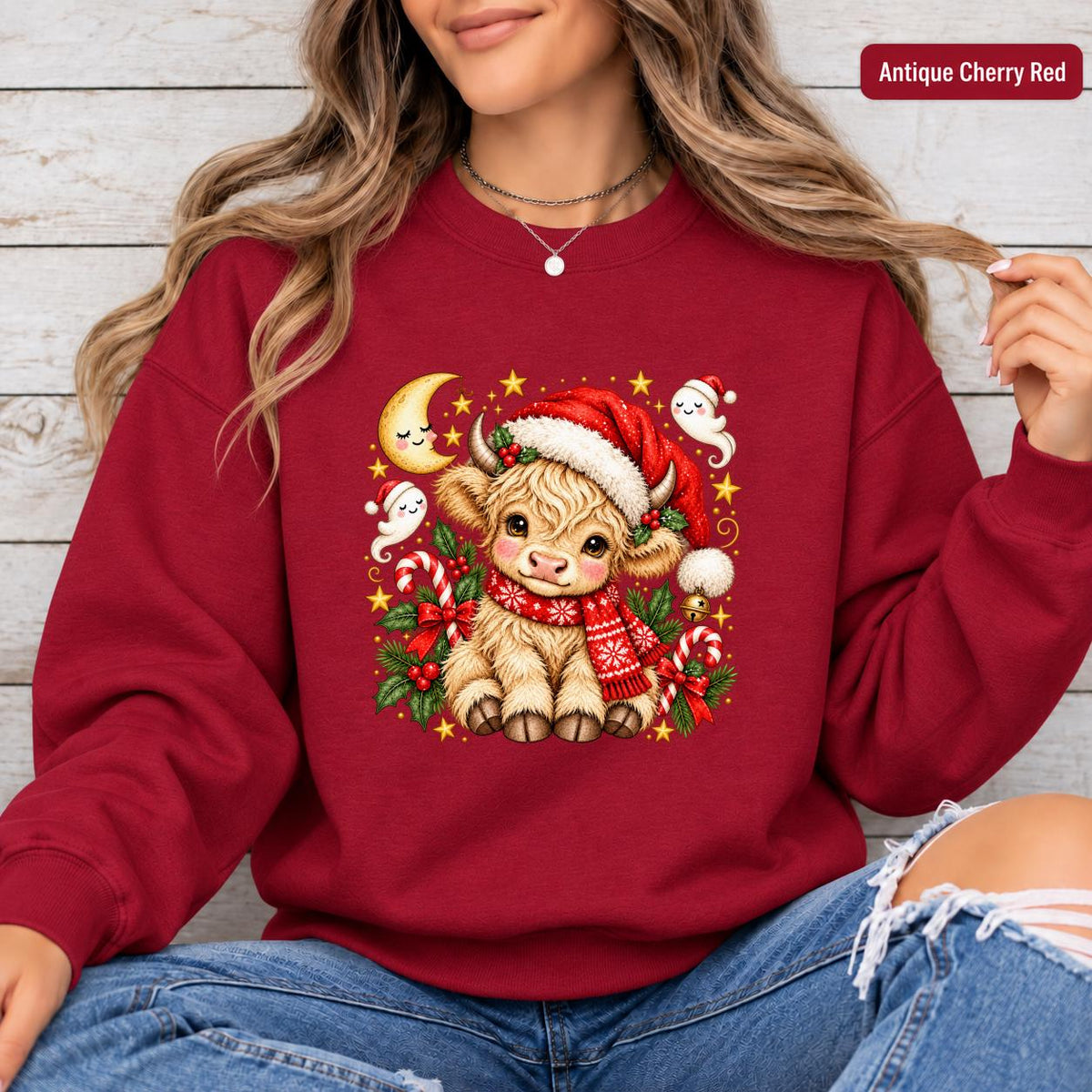 Antique Cherry Red Gildan sweatshirt featuring the Christmas Highland cow design with snowy scarf, Santa hat, holly, candy canes, and festive details.