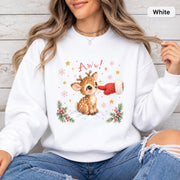 White Gildan 18000 crewneck displaying the adorable reindeer Christmas graphic with snowy accents, greenery, golden stars, and playful “Aww!” lettering.