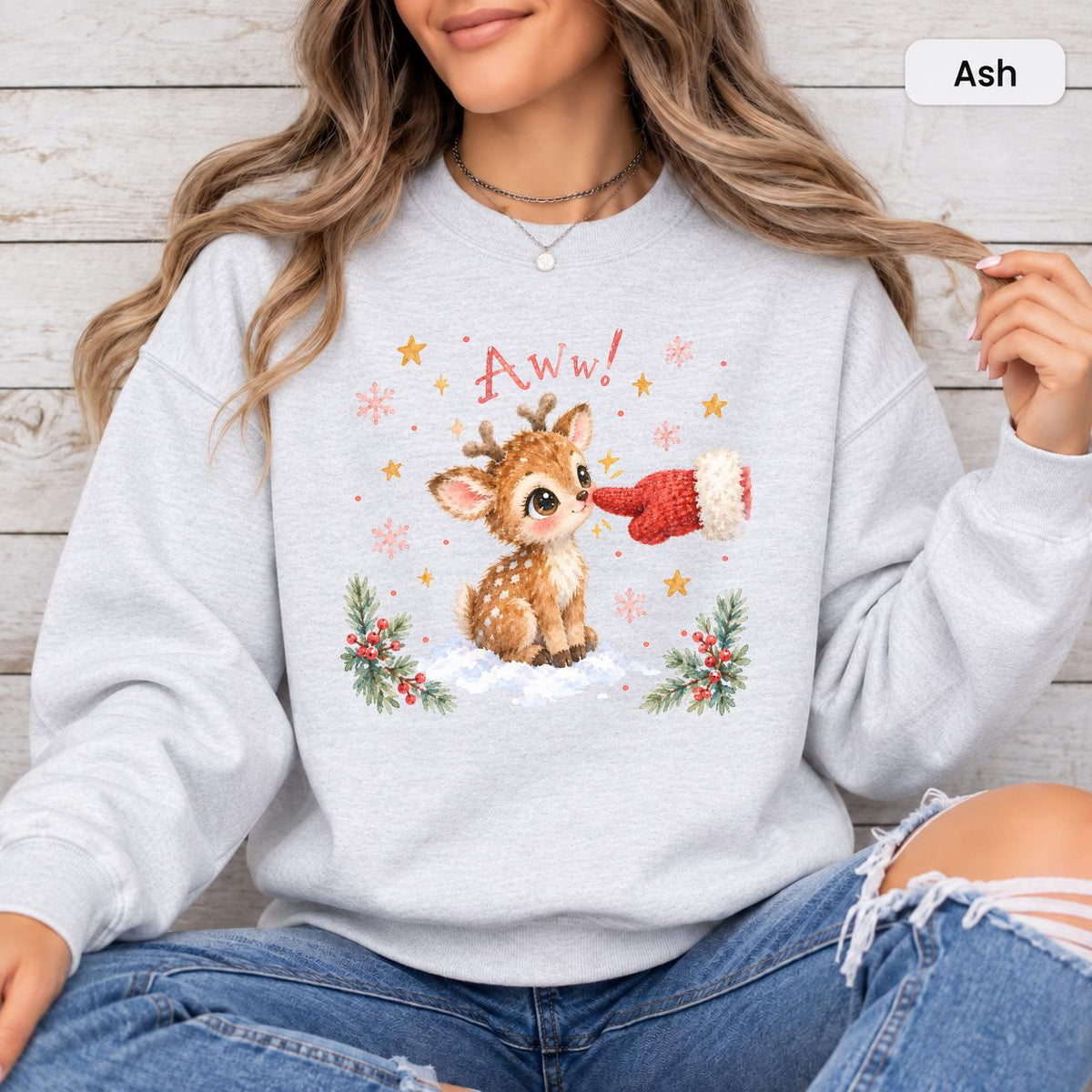 Ash Gildan 18000 crewneck showing the cute baby deer artwork with festive snow, evergreen branches, stars, and soft watercolor-style details.