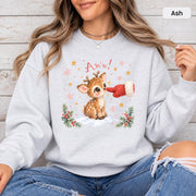 Ash Gildan 18000 crewneck showing the cute baby deer artwork with festive snow, evergreen branches, stars, and soft watercolor-style details.