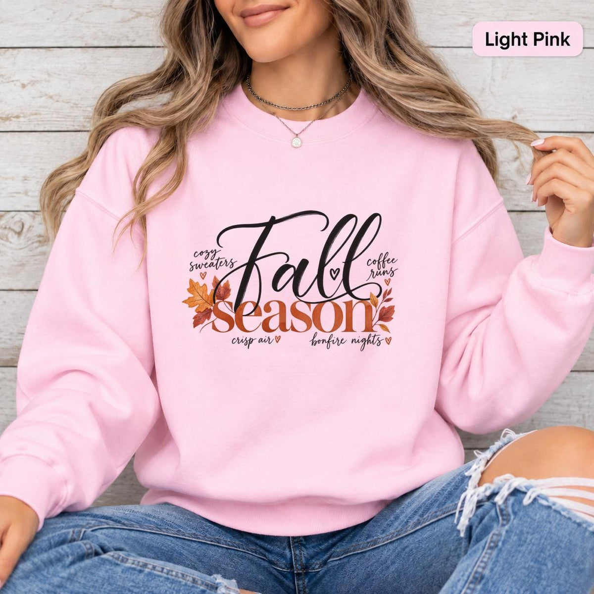 Light Pink Gildan 18000 sweatshirt featuring a Fall Season graphic with black script lettering, burnt orange leaves, and cozy autumn phrases.