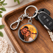 Personalized couple keychain displayed on a wooden tray beside car keys, showing the custom sunset photo and silver clip.