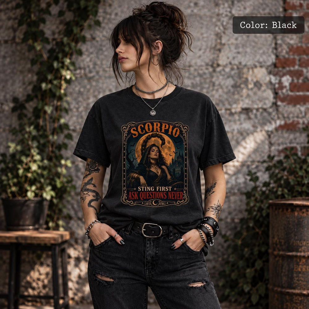 Woman wearing a Black Comfort Colors 1717 T-shirt featuring a gothic Scorpio zodiac graphic with a scorpion, orange celestial accents, and dark vintage artwork, styled with ripped black jeans.