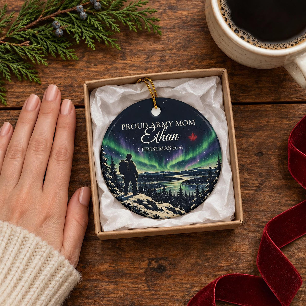 Personalized Army ornament shown at true size in a small kraft gift box beside a hand and a coffee mug, with cedar and a red velvet ribbon