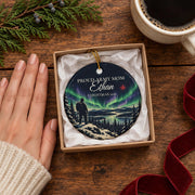 Personalized Army ornament shown at true size in a small kraft gift box beside a hand and a coffee mug, with cedar and a red velvet ribbon